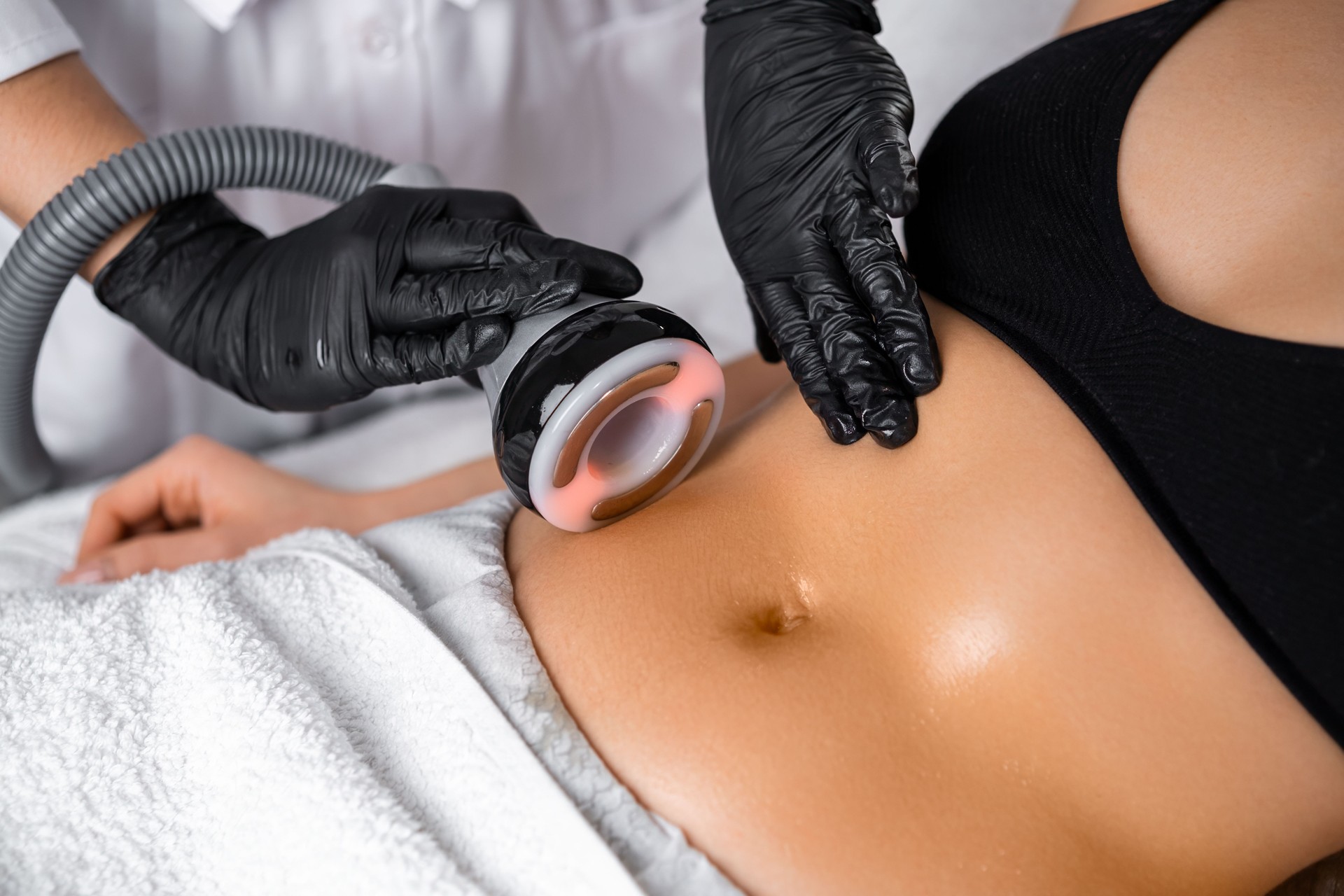 Close cosmetologist using ultrasound device while performing lifting procedure on woman belly